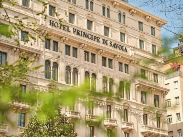 Historic façade of Hotel Principe di Savoia in Milan, Italy, viewed through spring greenery