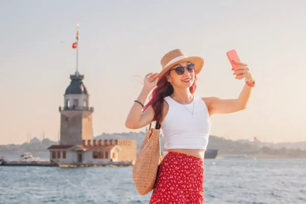 Travel influencer taking a selfie in front of Istanbul's Maiden's Tower on the Bosphorus during golden hour.