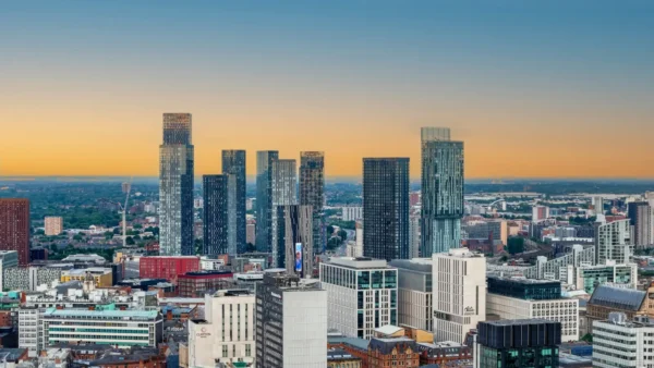 Home 6 Panoramic view of Manchester city centre skyline at sunset, featuring modern skyscrapers and high-rise buildings under a golden evening sky.