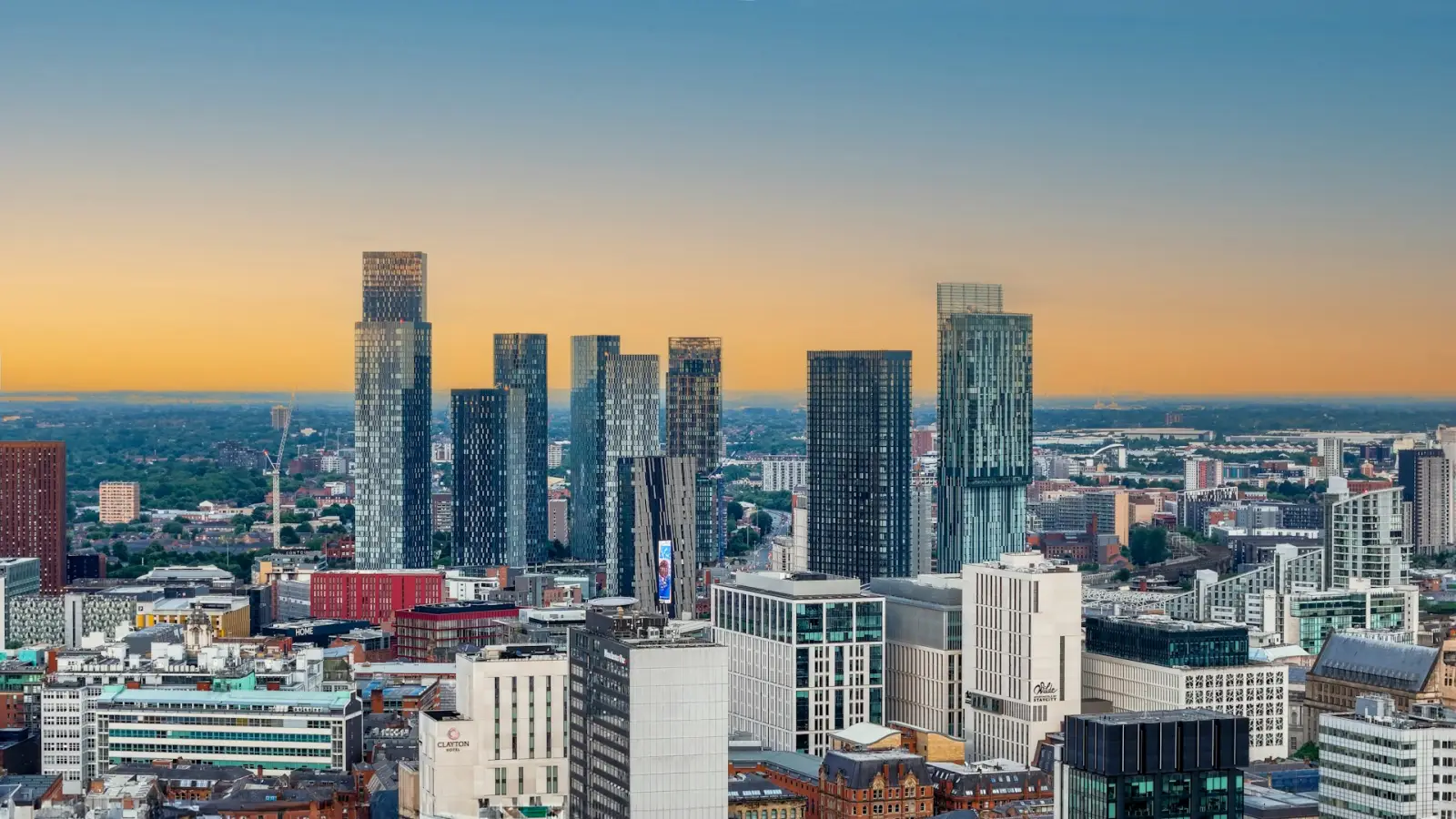 Panoramic view of Manchester city centre skyline at sunset, featuring modern skyscrapers and high-rise buildings under a golden evening sky.
