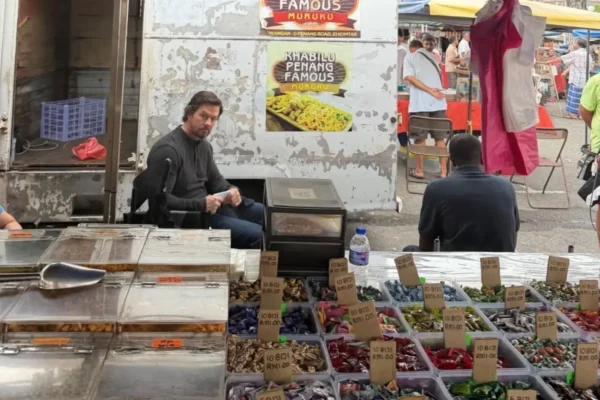 Mark Wahlberg sits beside a snack stall at a busy Penang market.