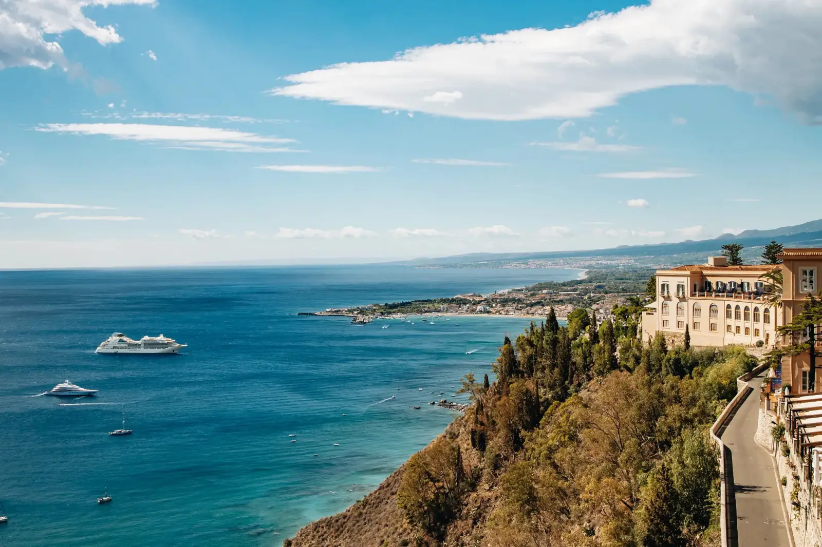 Seabourn Celebrates The Line’s 40Th Anniversary With 54 Special Voyages In 2028 4 A Seabourn cruise ship sails along the Mediterranean coast with scenic cliffs, coastal towns and luxury villas overlooking the sea.