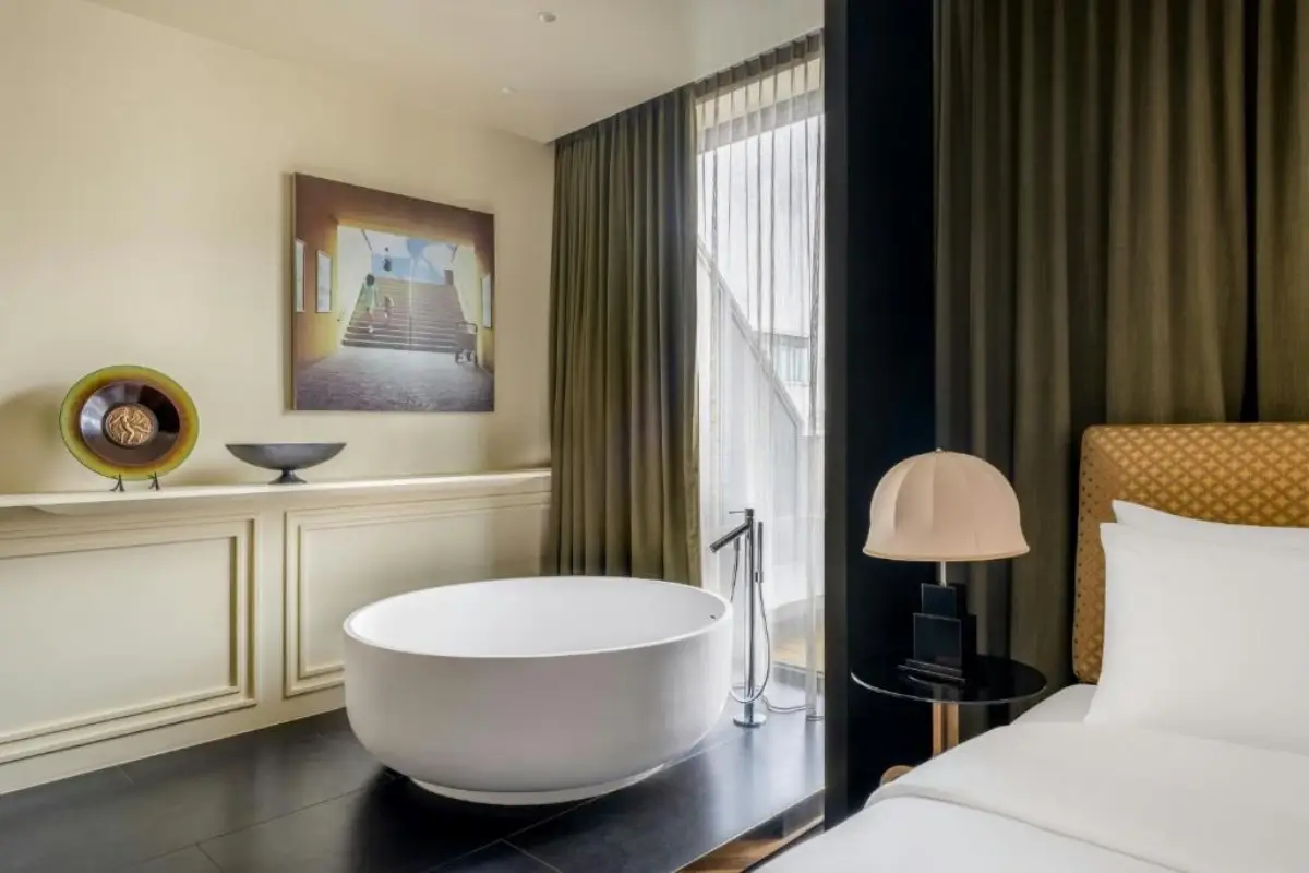 The Dean Opens Munich Hotel With 281 Rooms And Art Concept 3 A stylish guest room at The Dean Munich featuring a freestanding bathtub, contemporary furnishings, and floor-to-ceiling windows.