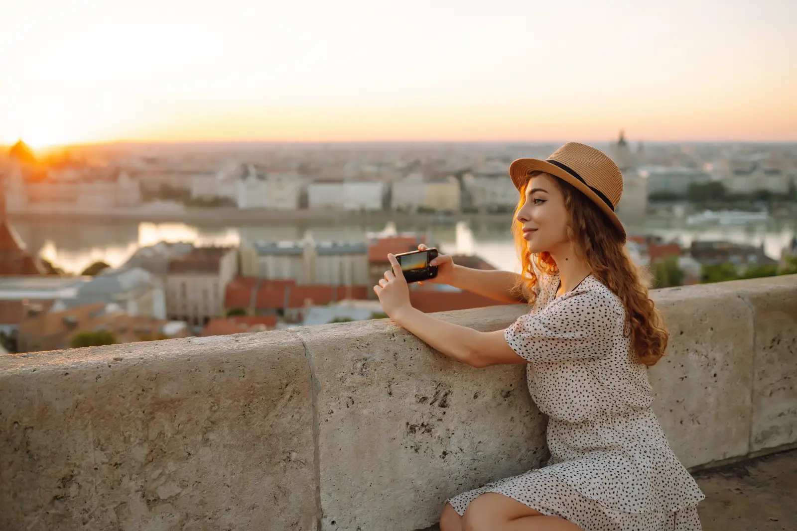 How Social Media Trends Are Influencing Travel Decisions In Istanbul In 2026 3 Young traveler taking a smartphone photo of a European city skyline at sunset from a scenic viewpoint.