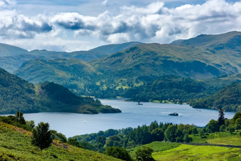 Tours 8 Panoramic summer view of Ullswater from Gowbarrow Fell in England's Lake District, with green hills, a blue lake, and scattered clouds.