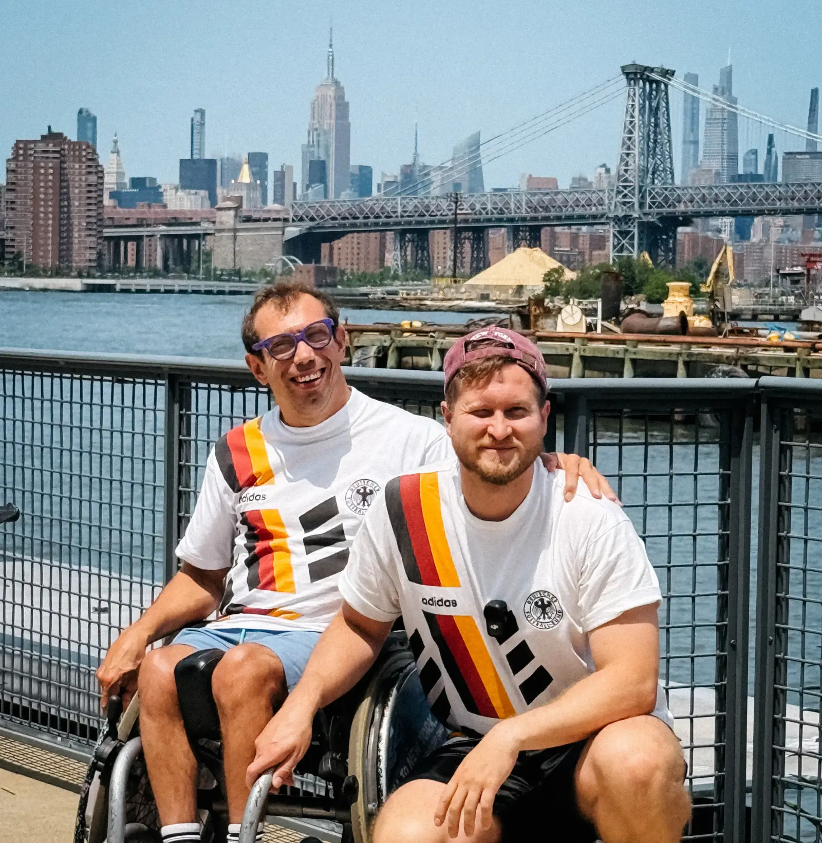 Wheelchair user and travel companion pose on the New York waterfront with the Manhattan skyline in the background